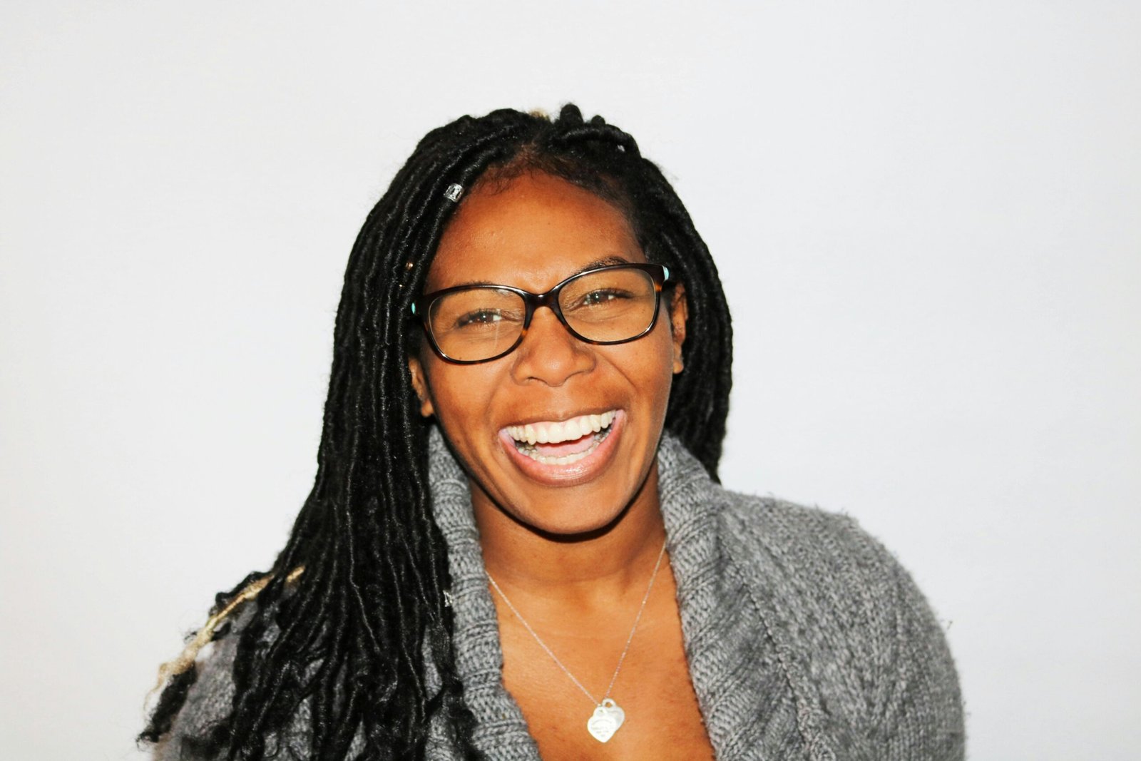 A vibrant portrait of a smiling woman with dreadlocks and glasses, exuding joy.